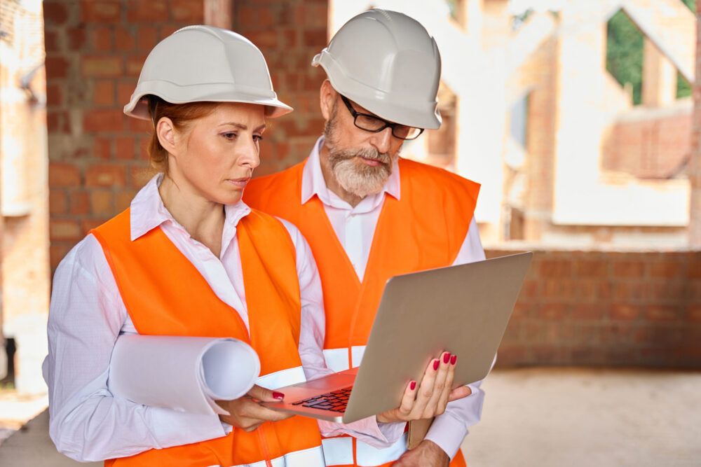 Engineer demonstrating data on computer to her colleague in unfinished dwelling house