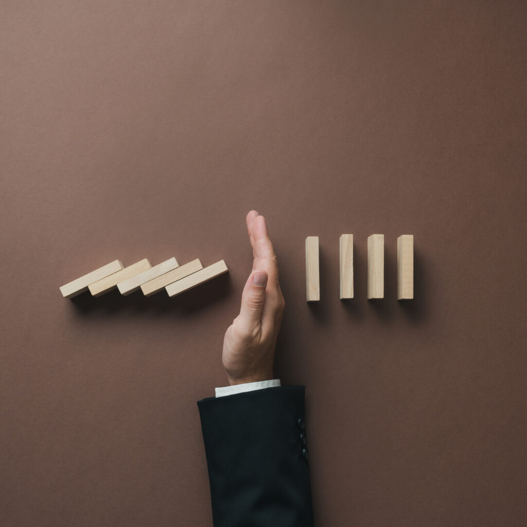 A hand stopping a row of falling wooden dominoes, representing how upgrading from Sage 50 to Sage 200 or Sage Intacct can help businesses scale efficiently.