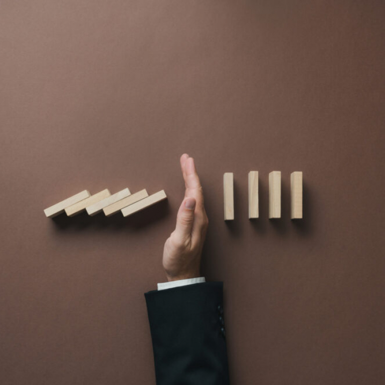 A hand stopping a row of falling wooden dominoes, representing how upgrading from Sage 50 to Sage 200 or Sage Intacct can help businesses scale efficiently.