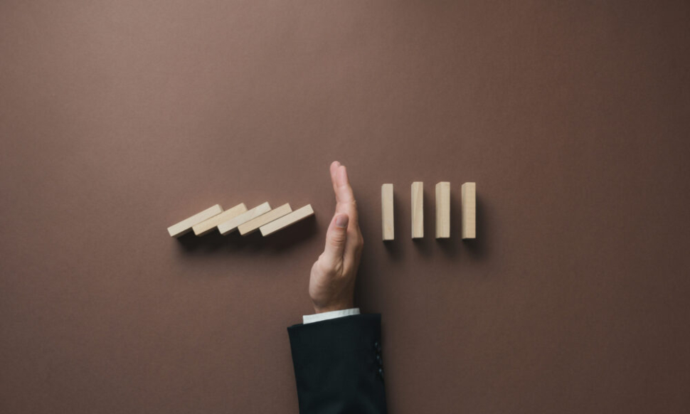 A hand stopping a row of falling wooden dominoes, representing how upgrading from Sage 50 to Sage 200 or Sage Intacct can help businesses scale efficiently.