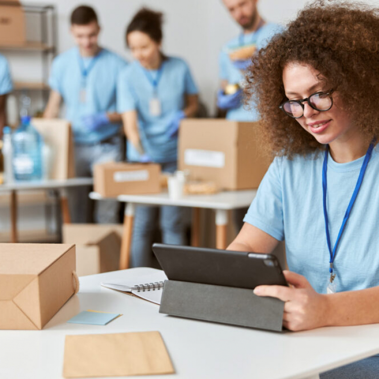 Young woman volunteer in blue uniform holding a laptop for UK charity finance management