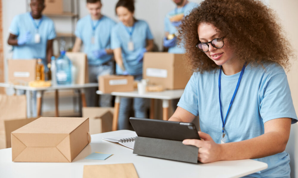 Young woman volunteer in blue uniform holding a laptop for UK charity finance management