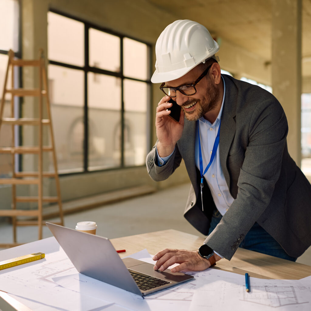 Engineer using Sage Intacct Construction accounting software on a laptop while talking on the phone at a construction site.
