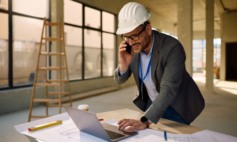 Engineer using Sage Intacct Construction accounting software on a laptop while talking on the phone at a construction site.