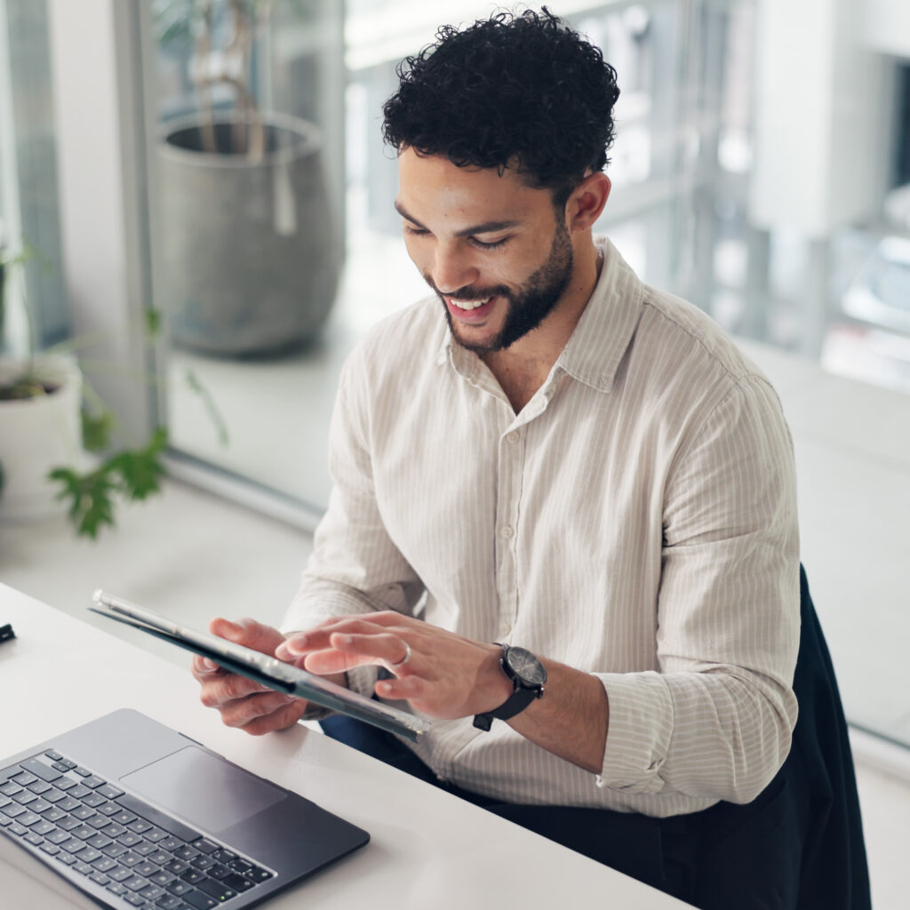 Business professional using a tablet and laptop in an office, reviewing Sage Intacct Professional Services automation software and project data.