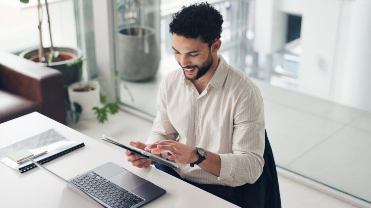 Business professional using a tablet and laptop in an office, reviewing Sage Intacct Professional Services automation software and project data.