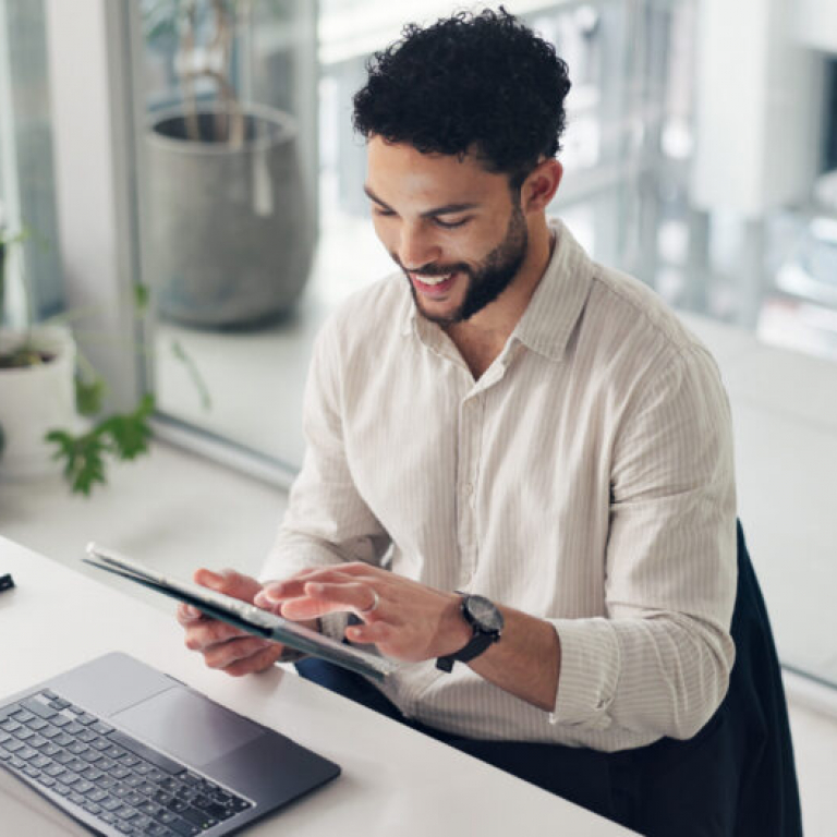 Business professional using a tablet and laptop in an office, reviewing Sage Intacct Professional Services automation software and project data.